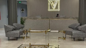 A modern reception area with a reception desk, two grey upholstered chairs, a decorative floor pattern, and a unique ceiling light fixture. - Voyage Serviced Apartments فوياج للشقق المخدومة (Riyadh)