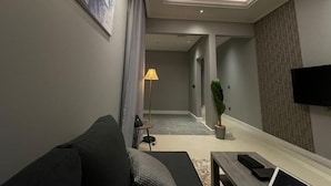A modern living room with a sofa, a coffee table, a lamp, and a TV. - Voyage Serviced Apartments فوياج للشقق المخدومة (Riyadh)