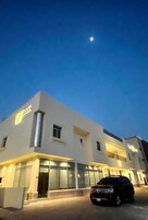 Um edifício moderno com fachada de vidro ampla, entrada visível e um carro estacionado em frente.