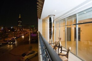 Uma varanda com vista para uma rua da cidade à noite, destacando um edifício com uma torre.