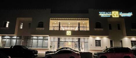 A building with a sign reading "VOYAGE AApartment" at night. There are cars parked in front.