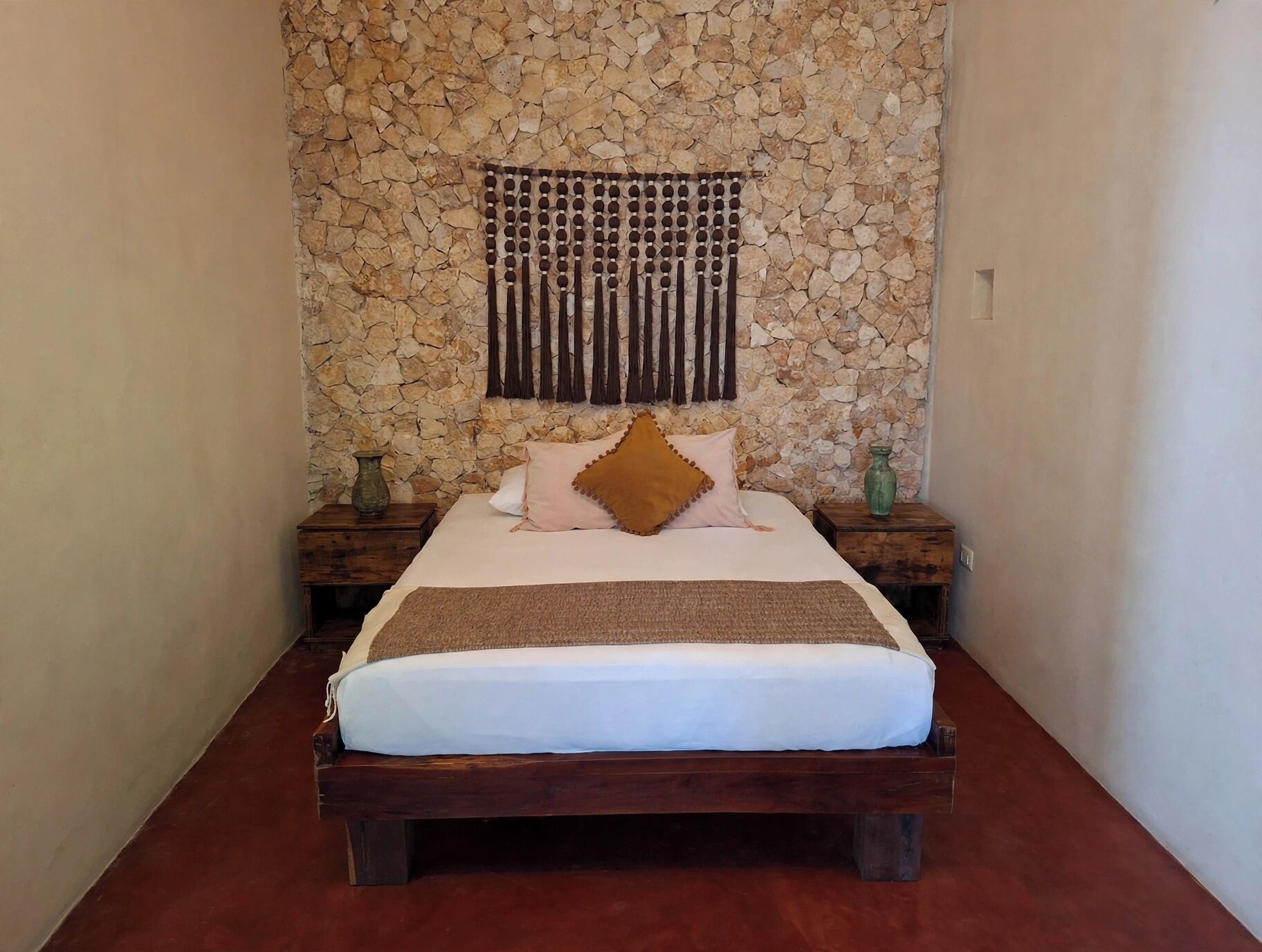 A bed with a wooden frame, a stone wall behind it, and a decorative hanging element.