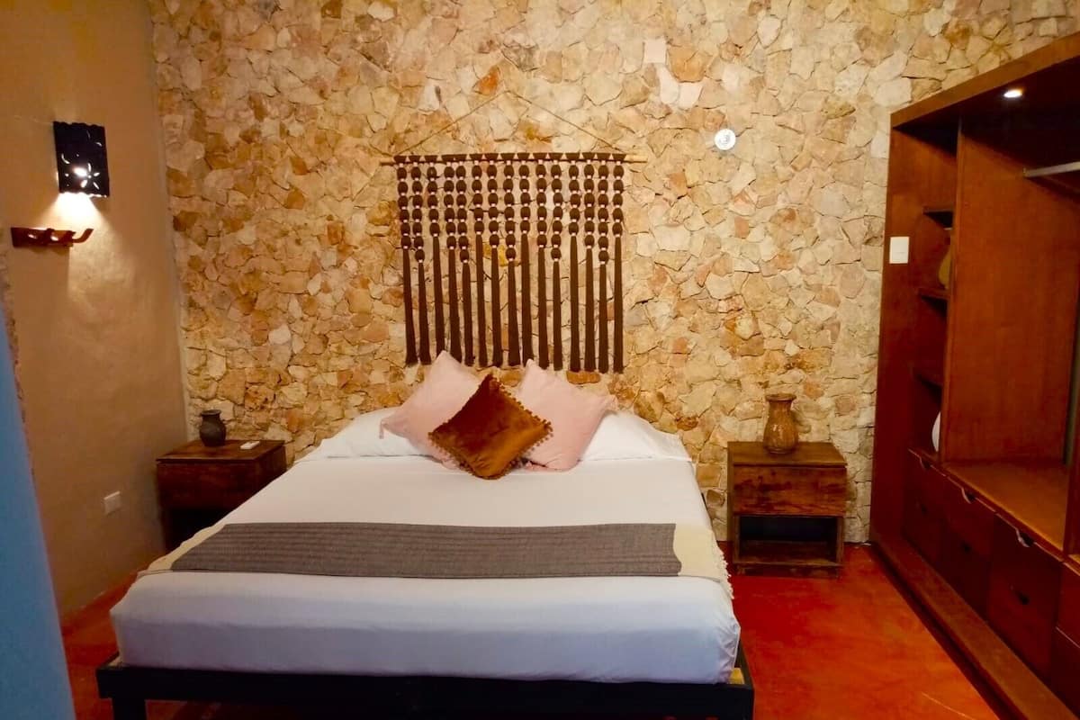 A bedroom with a stone wall, a bed with white bedding, a wooden headboard, and a red carpet.