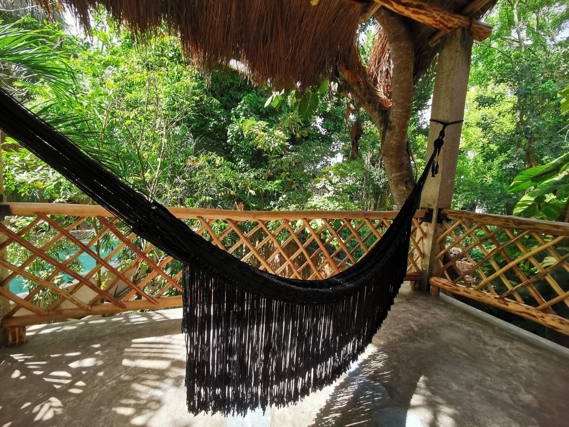 Una hamaca colgada entre vigas de madera en un balcón con vistas a exuberante follaje.