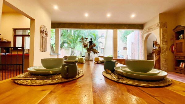 Un comedor con una mesa de madera dispuesta para una comida, rodeada de sillas y cuencos.