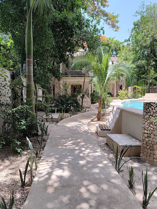 A pathway leading to a pool area surrounded by lush greenery and a stone wall. - Hotel Refugio 41 (Valladolid)