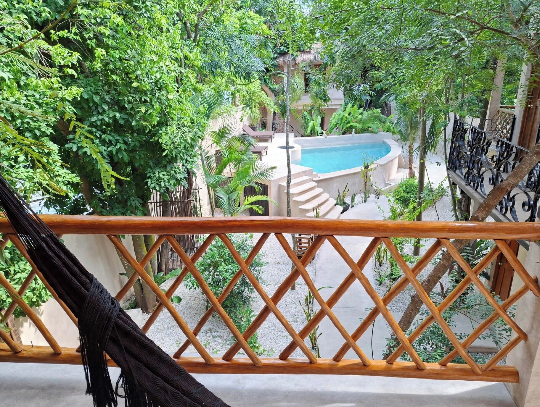 A hammock on a balcony overlooking a swimming pool surrounded by lush greenery.