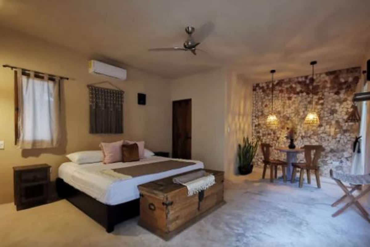 A bedroom with a bed, a chest of drawers, a ceiling fan, a stone wall, and a small table with chairs.