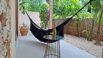 A hammock chair with a glass table, a potted plant, and a stone wall in a garden setting.