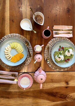 A wooden table with two plates of food, a pink teapot, a pink cup, a spoon, a fork, and a napkin. - Hotel Refugio 41 (Valladolid)