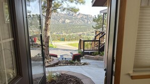 A door leading to a covered outdoor area with a view of a mountain, a wooden deck, and a stone pathway.