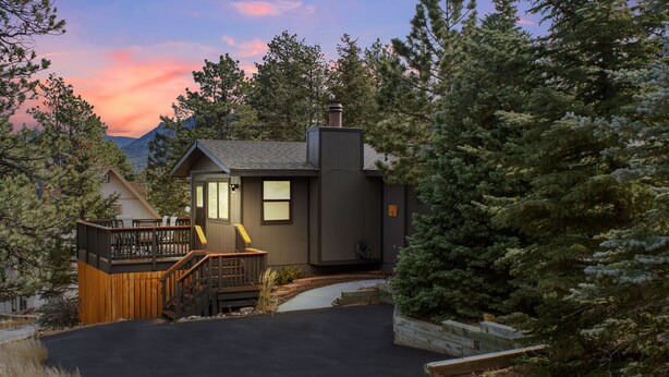 A cabin with a deck, a chimney, and a view of mountains.