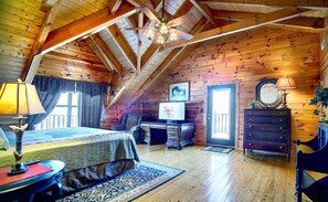 A cozy attic bedroom with a bed, desk, dresser, and a ceiling fan.