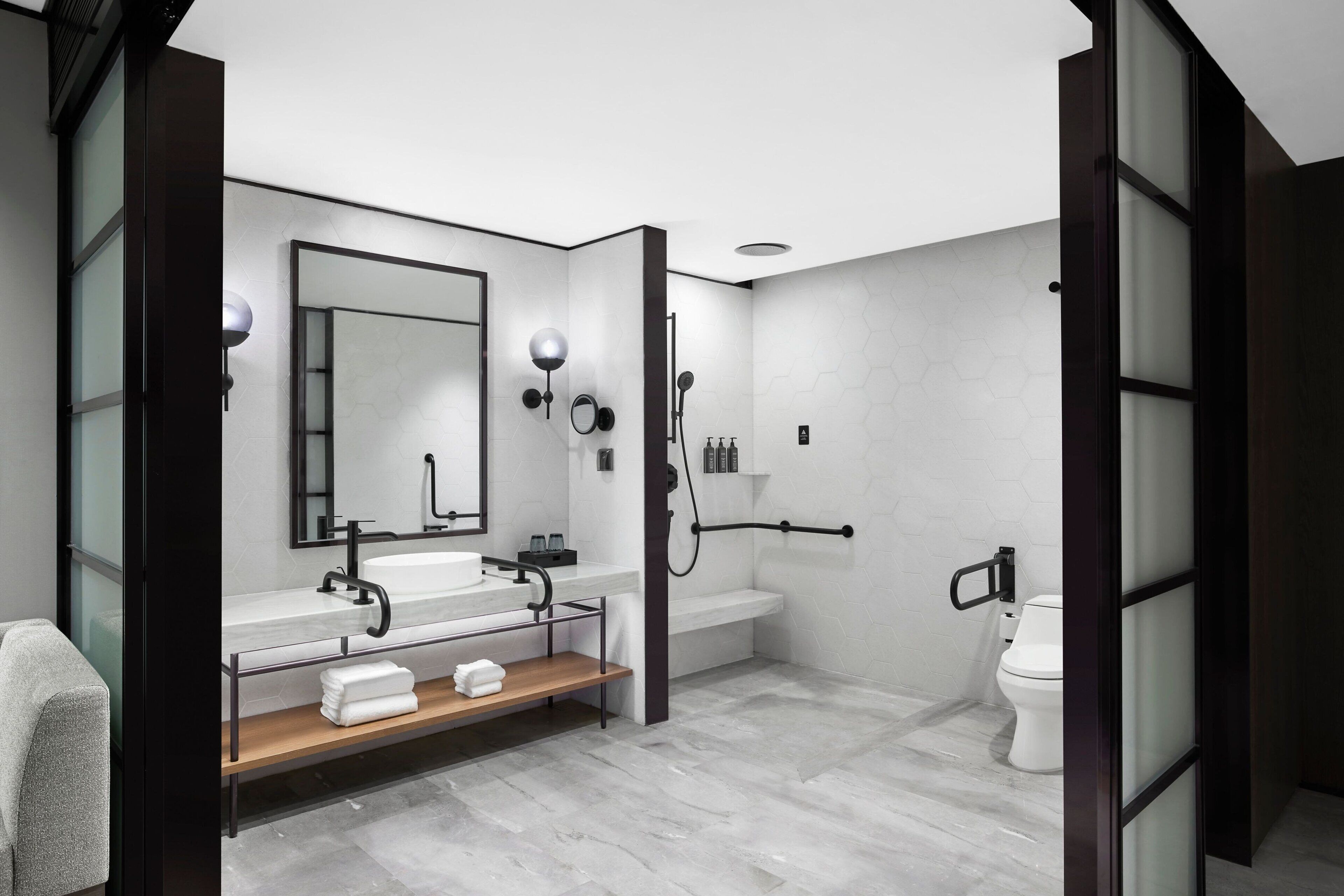 A modern bathroom with a large mirror, two sinks, a shower, and a toilet.