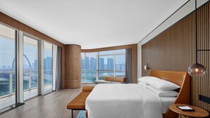 A modern hotel room with a large bed, a bench, a small table, and a view of the city skyline through large windows. - Sheraton Zhaoqing Dinghu (Zhaoqing)