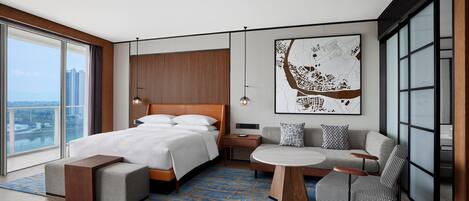 A modern hotel room with a large bed, a sofa, a coffee table, and a city view.