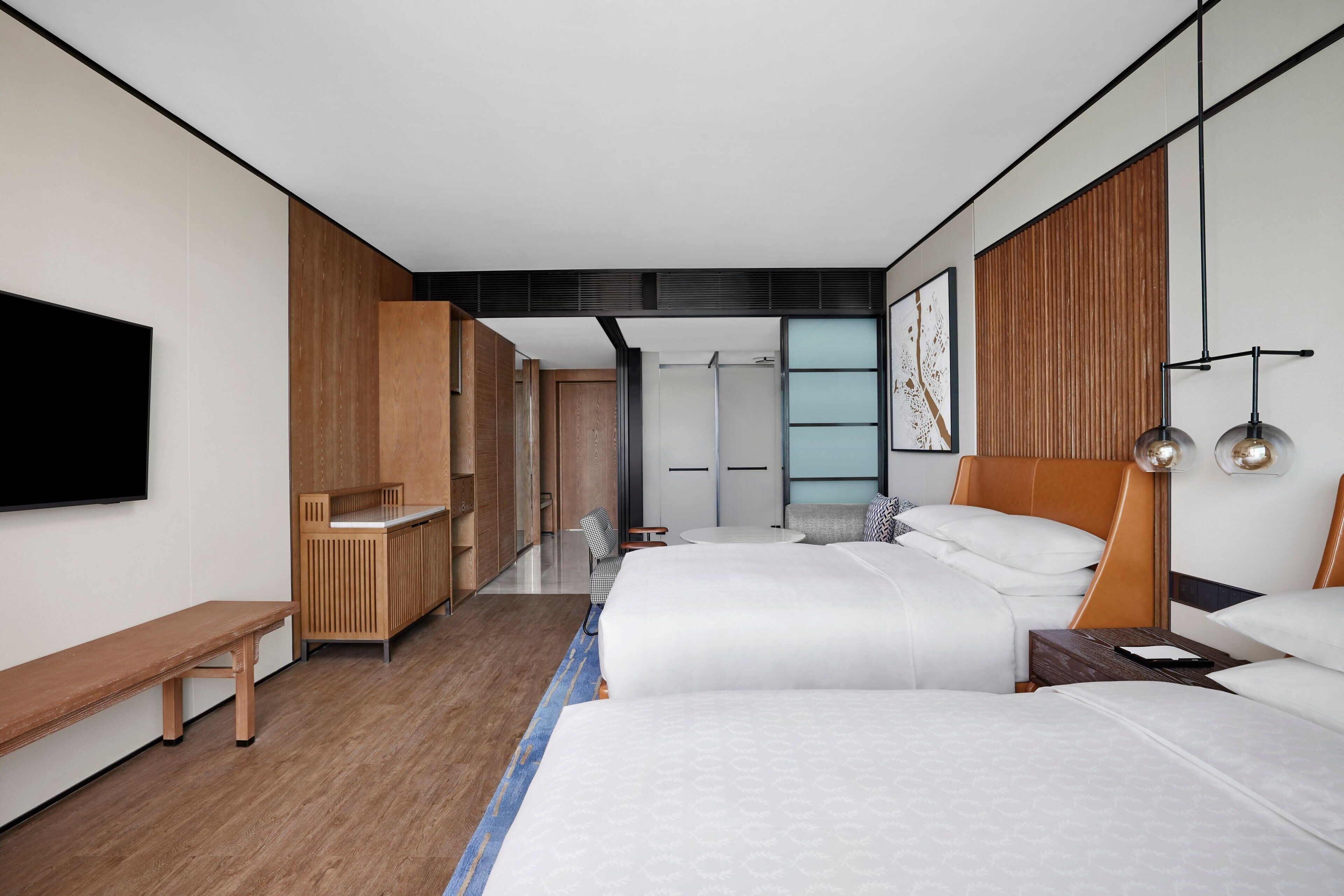 Una habitación de hotel moderna con dos camas, un banco, un escritorio y una televisión.