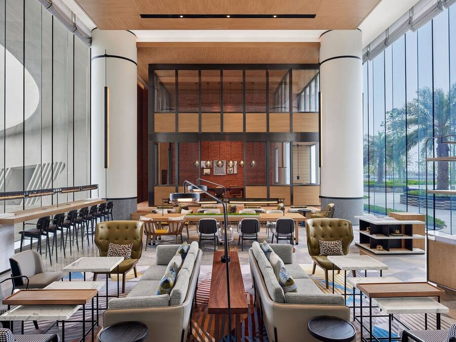 A spacious lobby with a central seating area, large windows, and a view of palm trees.