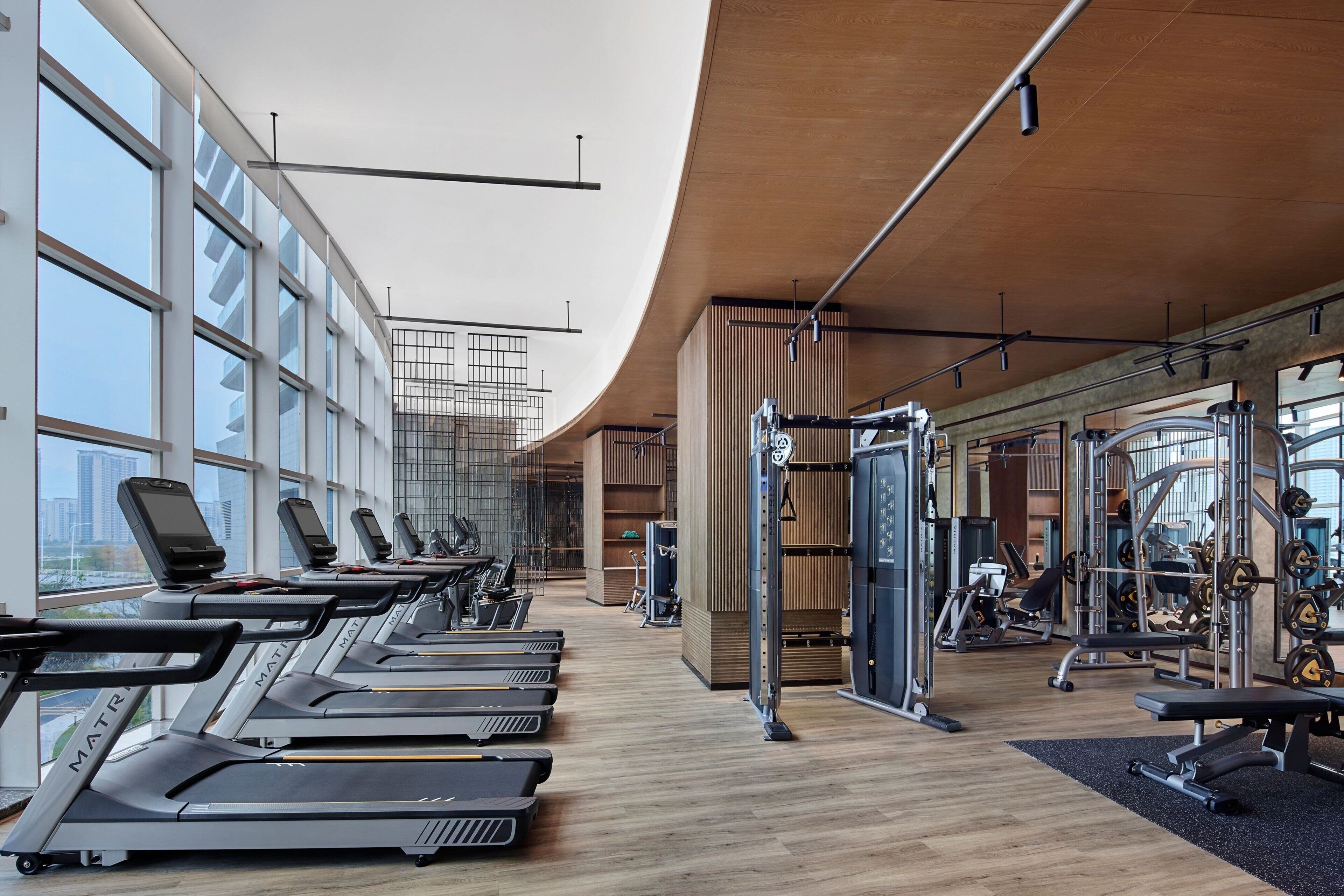A modern gym with treadmills, weight machines, and a large window offering a city view.