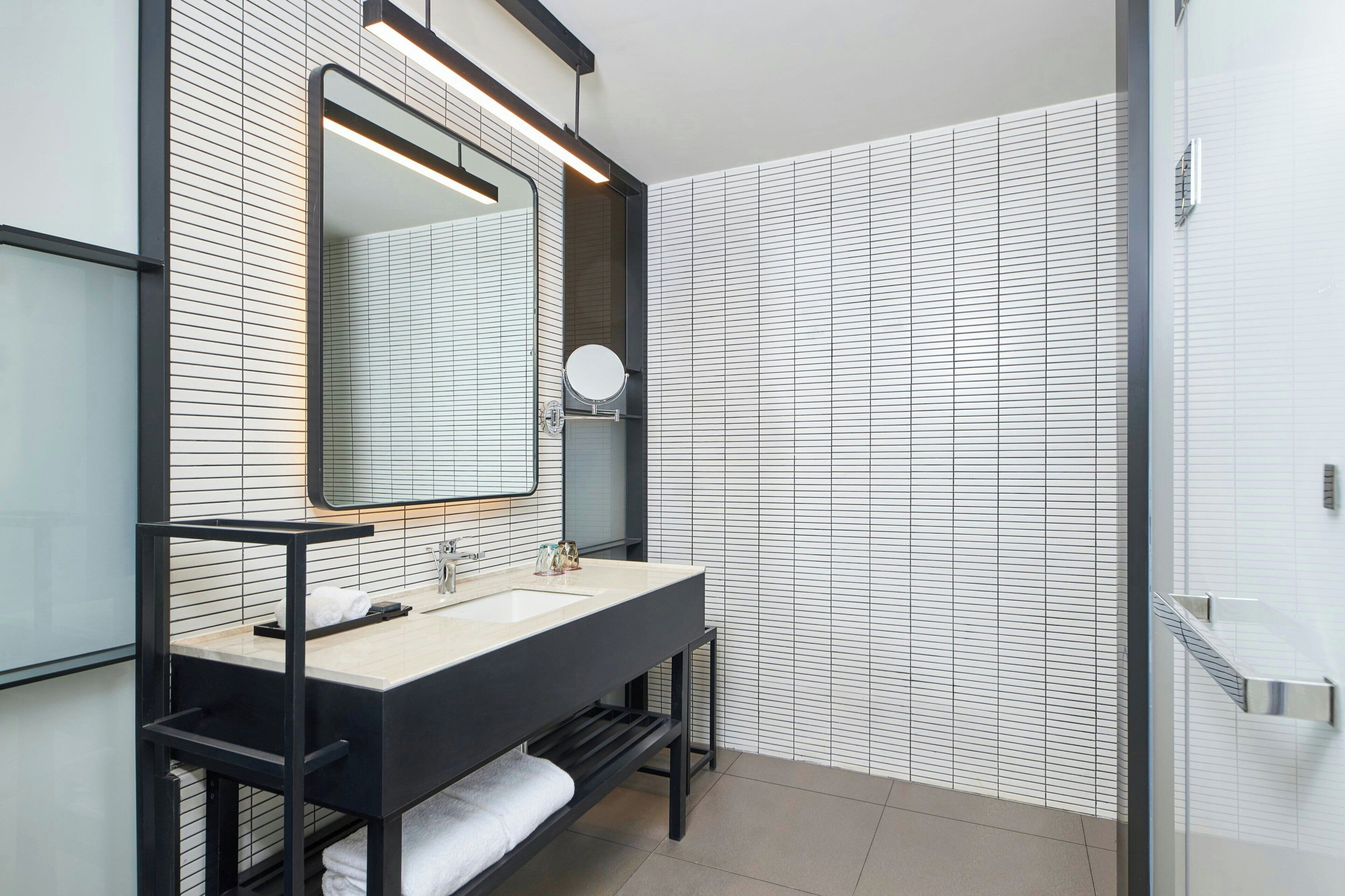 Un baño moderno con tocador negro, un espejo grande y pared con azulejos.