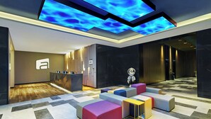 A modern lobby with a reception desk, colorful seating areas, and a ceiling with illuminated panels. - Aloft Shijiazhuang (Shijiazhuang)