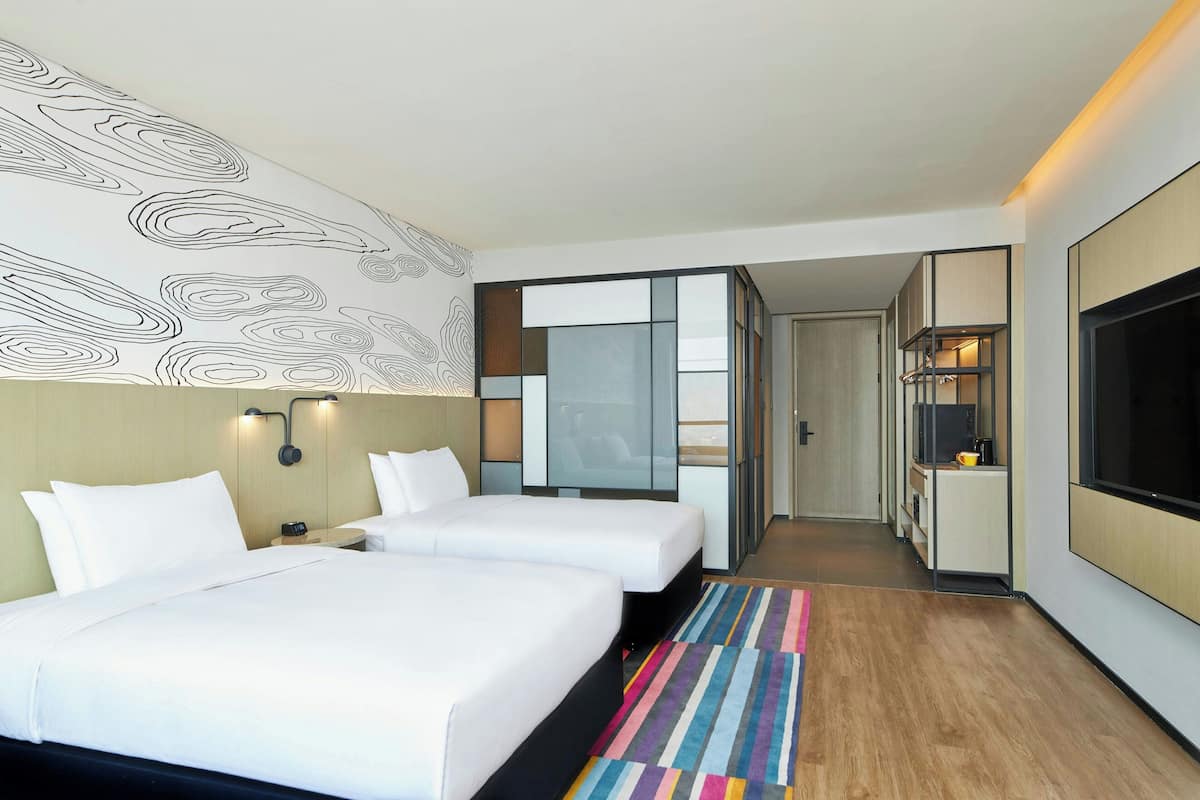 Une chambre d’hôtel avec deux lits, une grande télévision, un minibar et une vue sur le couloir.
