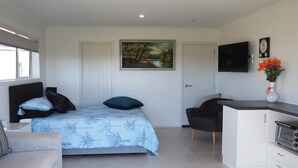 A modern bedroom with a bed, a sofa, a desk, and a TV. - Paradise on the Sand (Whakatane)