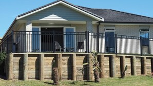 A single-story house with a covered porch, a fenced deck, and a brick foundation. - Paradise on the Sand (Whakatane)