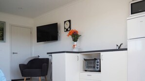 A compact kitchen with a built-in oven, a flat-screen TV, and a small refrigerator. - Paradise on the Sand (Whakatane)
