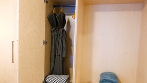 A bedroom with a wooden wardrobe, a bed, and a small shelf with folded clothes. - Private Suite & Hot Tub @ Red (Rossland)