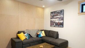 A modern living room with a gray sectional sofa, a wooden coffee table, and a large framed picture on the wall. - Private Suite & Hot Tub @ Red (Rossland)