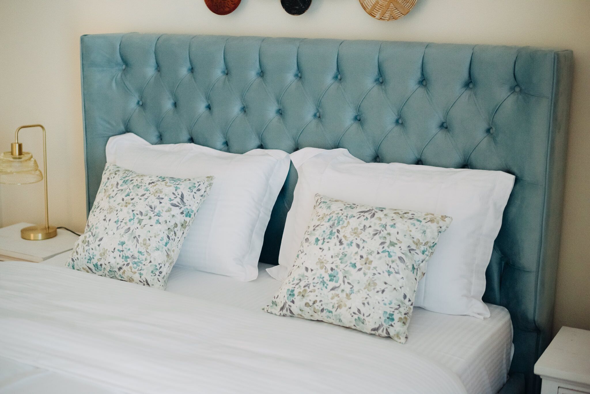 A bed with a tufted headboard, white bedding, and floral-patterned pillows.