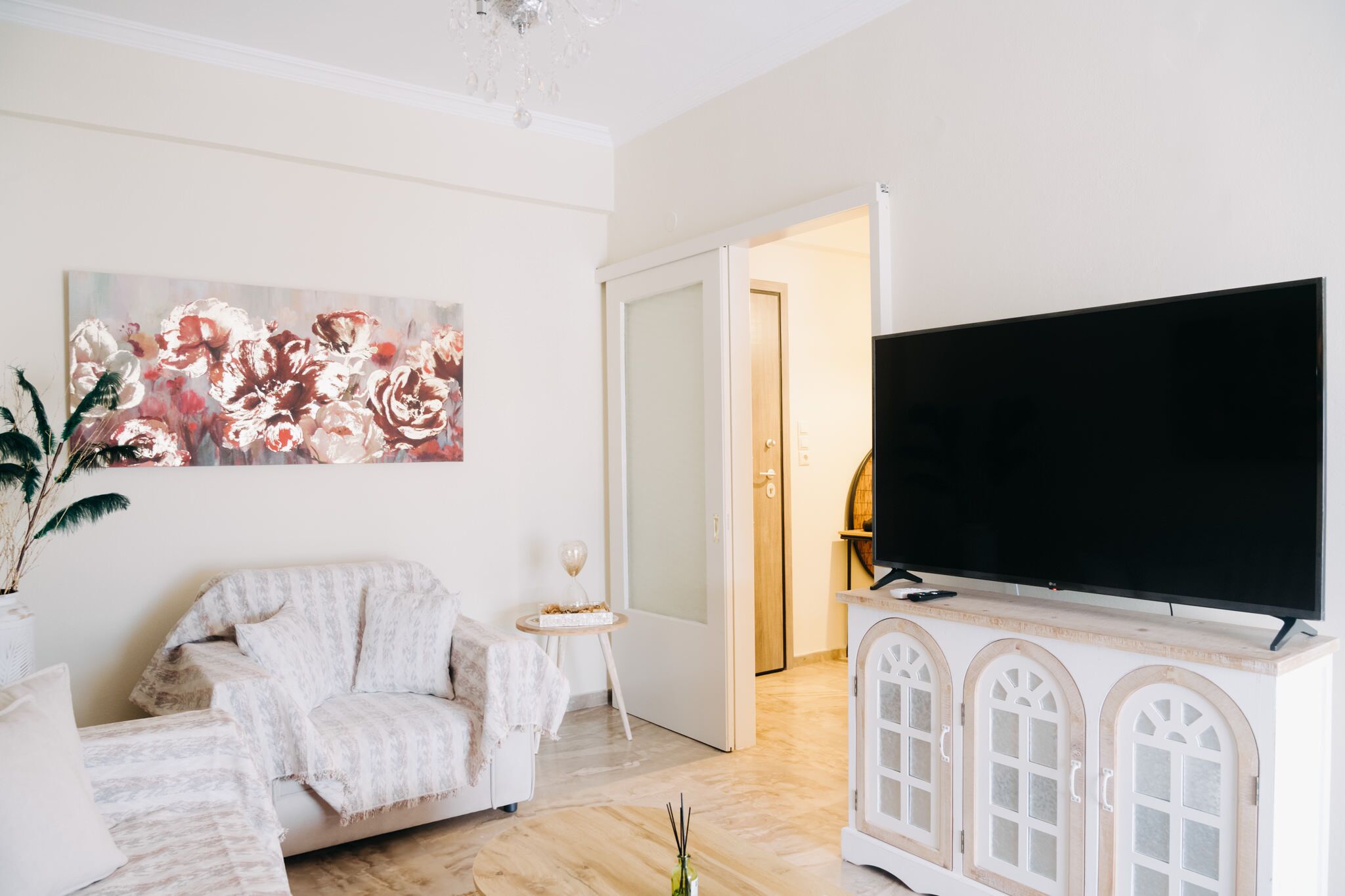 Una sala de estar con un sofá, un televisor de pantalla plana sobre un mueble bajo, un cuadro en la pared y una puerta que da a otra habitación.