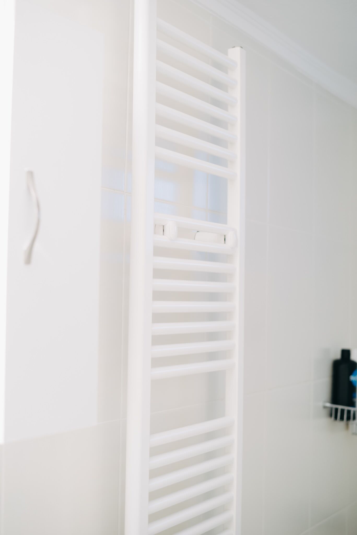 A white radiator in a bathroom with white walls and a white towel rack.