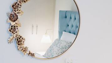 A white dresser with a gold-framed mirror and a small white vase with flowers.