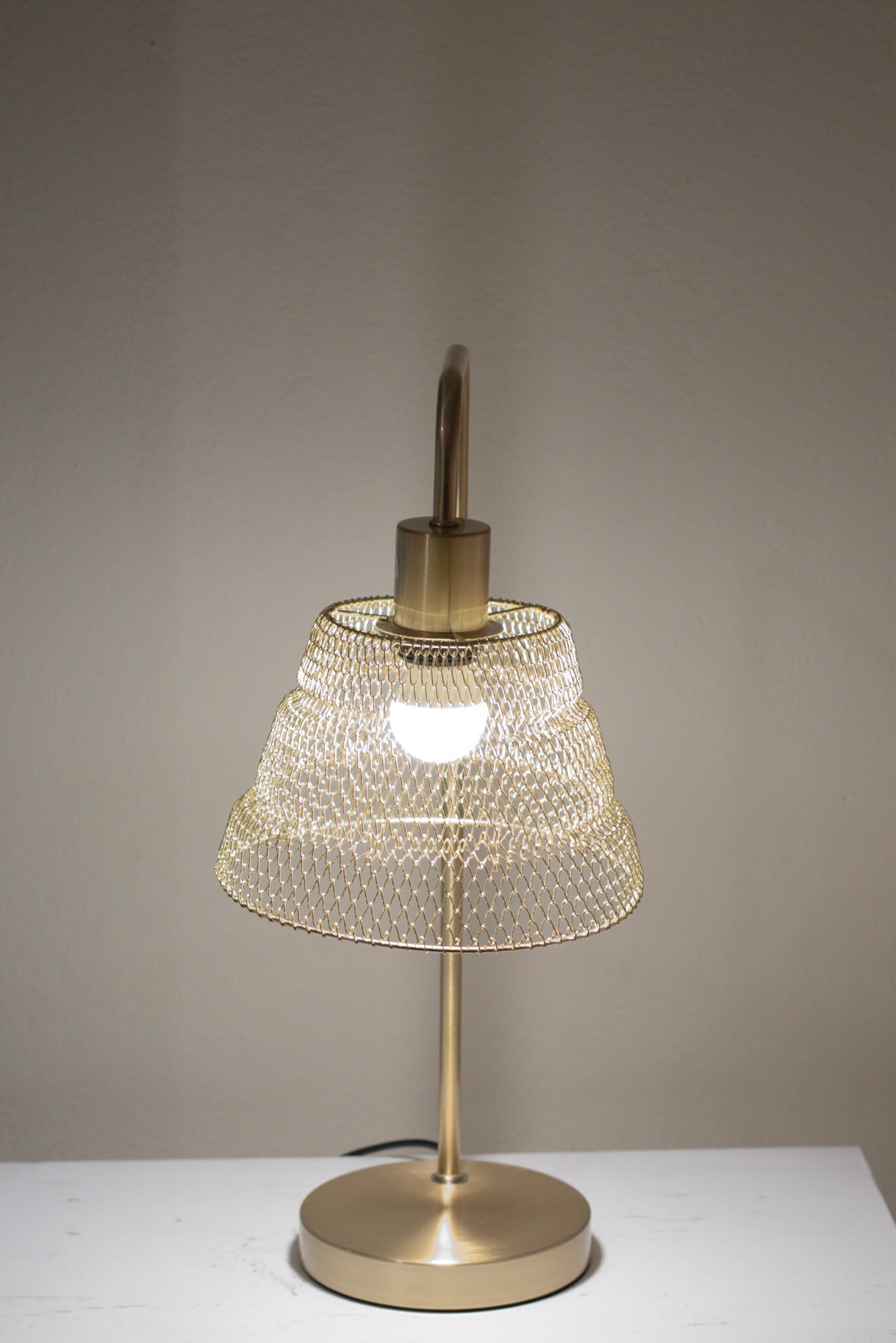 Eine Tischlampe mit goldfarbenem Sockel und einem Drahtschirm.