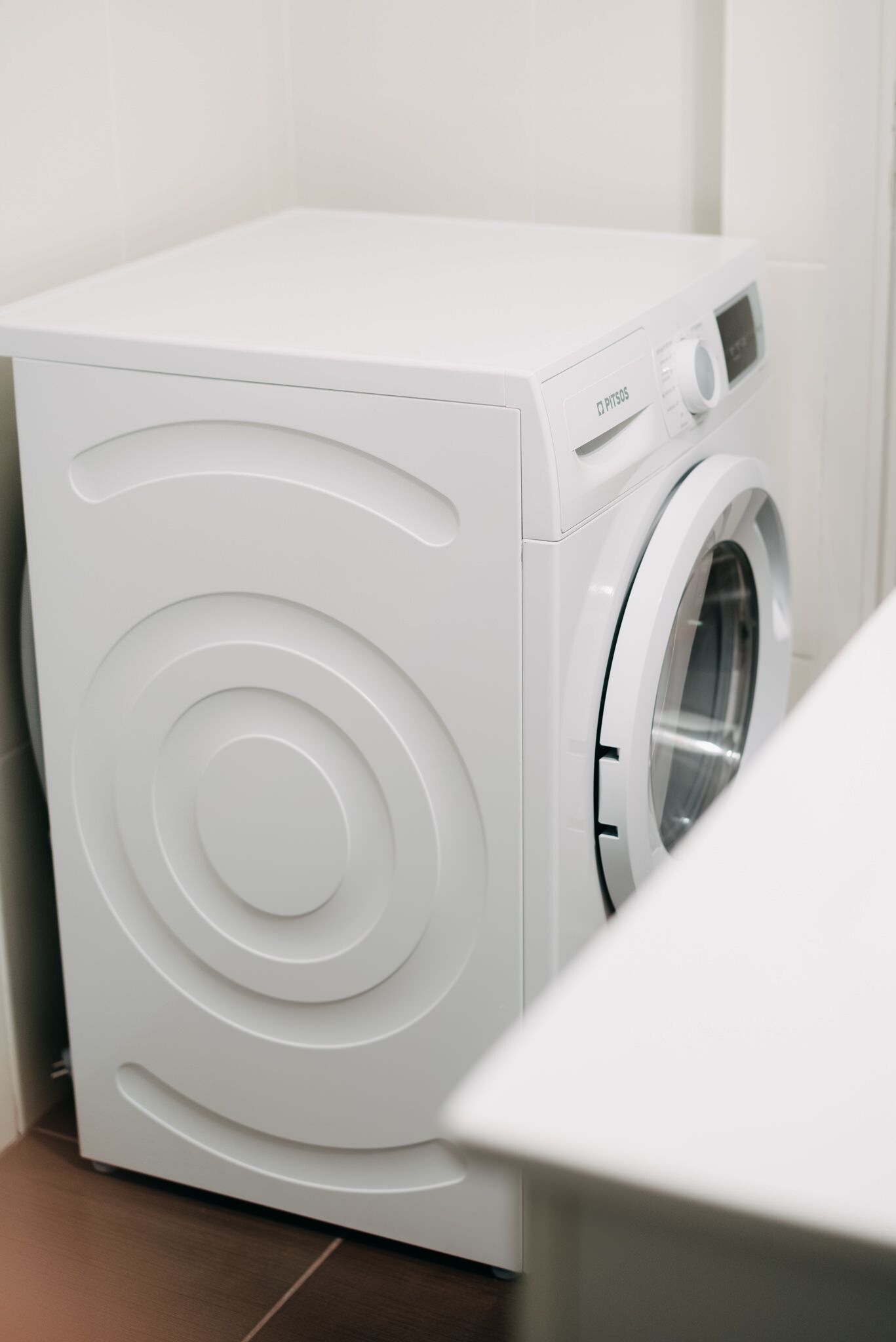 Una lavadora blanca de carga frontal, compacta, en un baño con piso de baldosas.