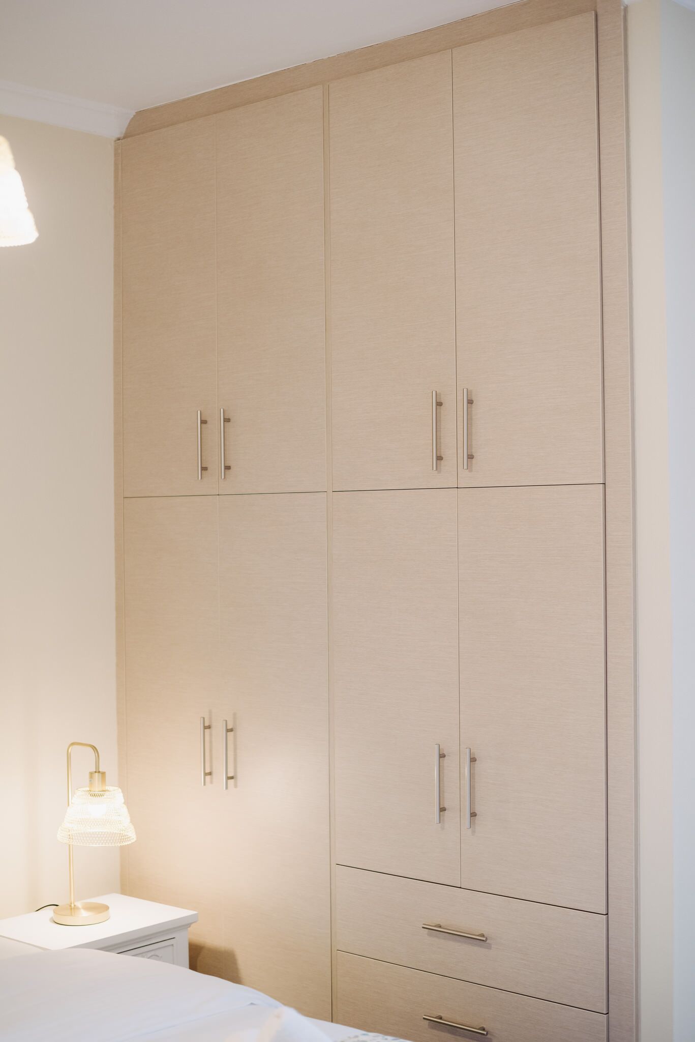 A bedroom with a large wardrobe, a bedside table with a lamp, and a bed.