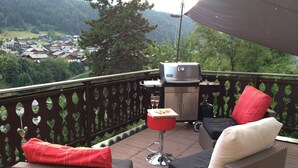 A balcony with wicker furniture, a grill, and a view of a village. - View and Location! (Morzine)