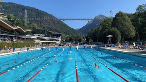 A swimming pool with multiple lanes, surrounded by buildings and a mountainous backdrop. - View and Location! (Morzine)