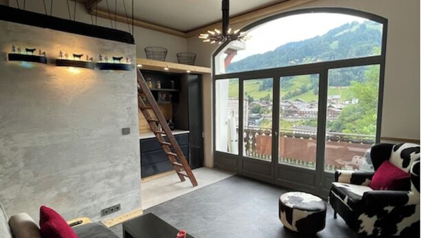 A modern living room with a large window, a sofa, a coffee table, and a cow-patterned chair. - View and Location! (Morzine)