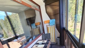 Un balcon avec une table et des chaises, une vue sur les arbres et une fenêtre avec des stores.