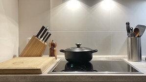 Een moderne keuken met een fornuis, een pan op de inductiekookplaat en een houten snijplank.
