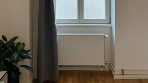 Een kamer met een groot raam, een radiator eronder en een potplant aan de linkerkant.