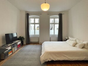 A bedroom with a bed, a TV, a bookshelf, and two windows with curtains. - Stylish & Central 1-Bedroom Apt. in Quiet Mitte (Berlin)