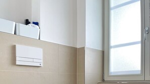 Een moderne badkamer met een wit toilet, een toiletrolhouder en een wandairconditioning.