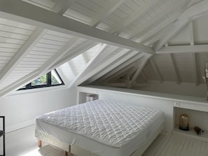 Un dormitorio con techo inclinado, una cama, una mesita y un ventanal.