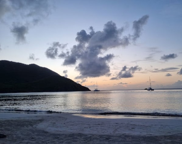 Una playa con aguas tranquilas, barcos y un paisaje montañoso.