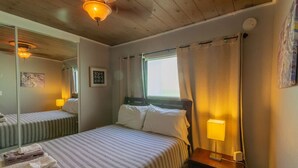 Een hotelkamer met een bed, een bedlamp, een raam met gordijnen, een spiegel en een schilderij aan de muur.