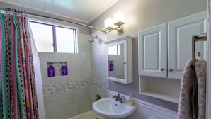 Een badkamer met een bad, een wastafel, een douche en een spiegel.